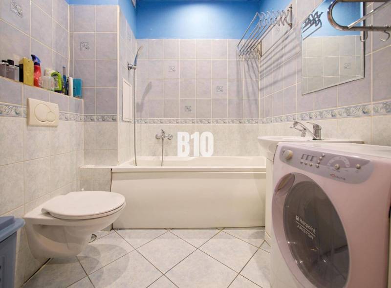 A bathroom in a 2-room apartment with a shower, sink, and washing machine.