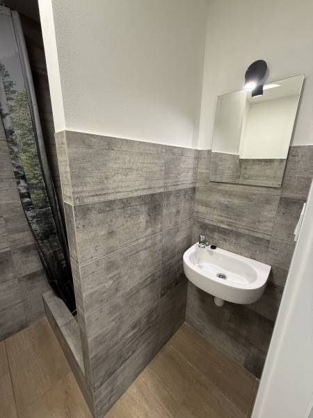 Studio apartment with gray tiles and a mirror, sink, floor with wood decor.
