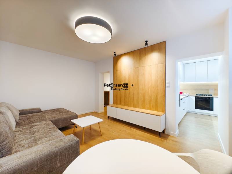 Living room in a two-room apartment with a wooden decor floor, entrance to a white kitchen.