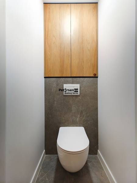A bathroom in a 2-room apartment with a dark stone floor and wooden cabinets.