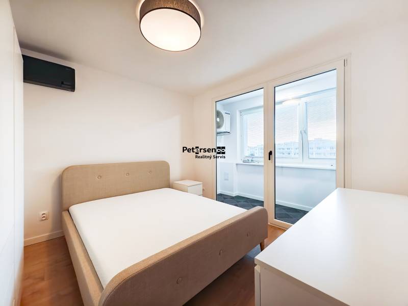 Bedroom in a two-room apartment with a bed, table, and balcony, wooden decor flooring.