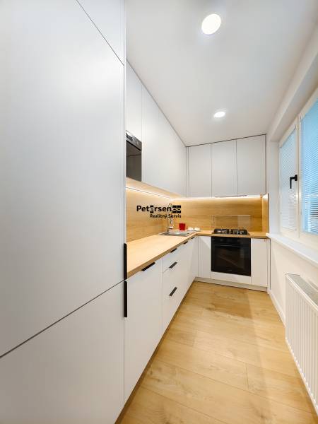 A kitchen in a 2-room apartment with a white kitchen unit and a floor with a wood decor.