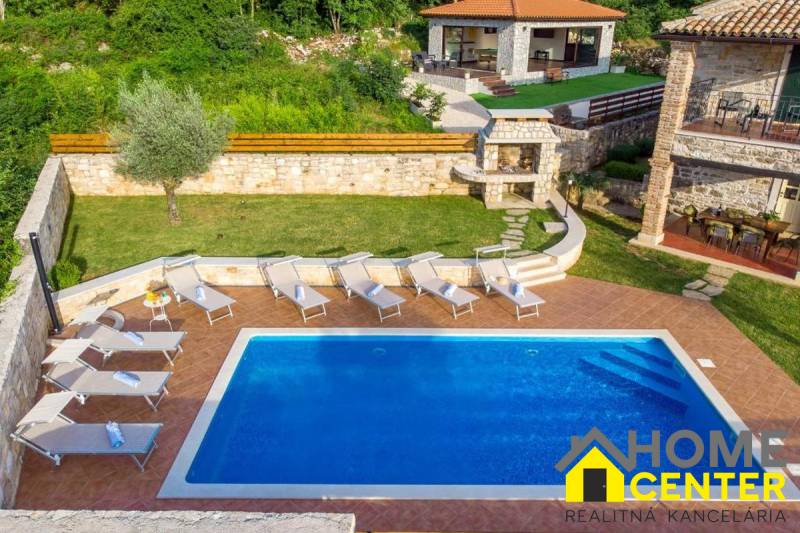 A villa in the town of Bale with a pool, sun loungers, and a stone seating area surrounded by greenery.