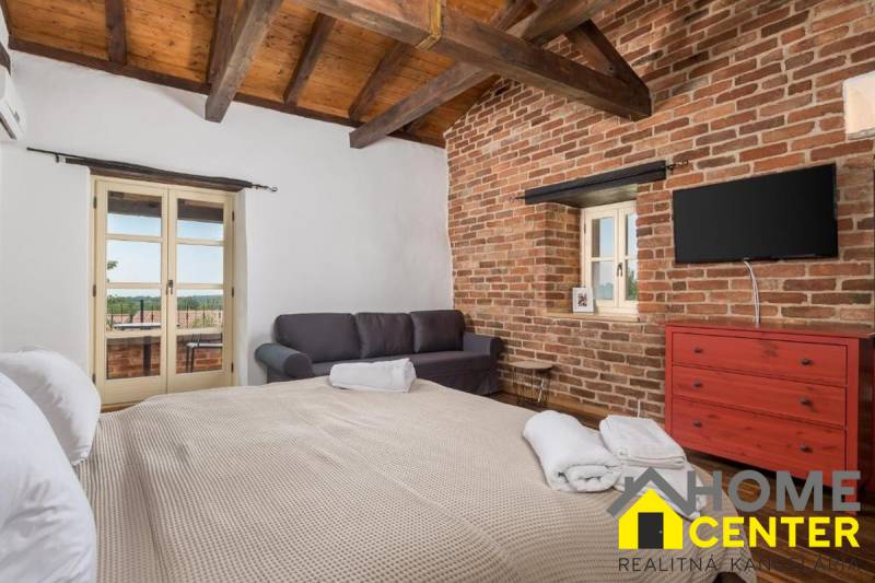 A bedroom in a villa with brick walls, a TV, a sofa, and a large bed.