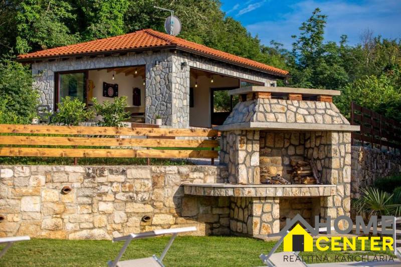 Stone facade and outdoor fireplace at the villa in Bale, surrounded by greenery and trees.