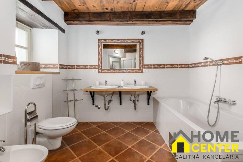 Bathroom in a villa with white walls, bathtub, sinks, and floor with wooden decor.