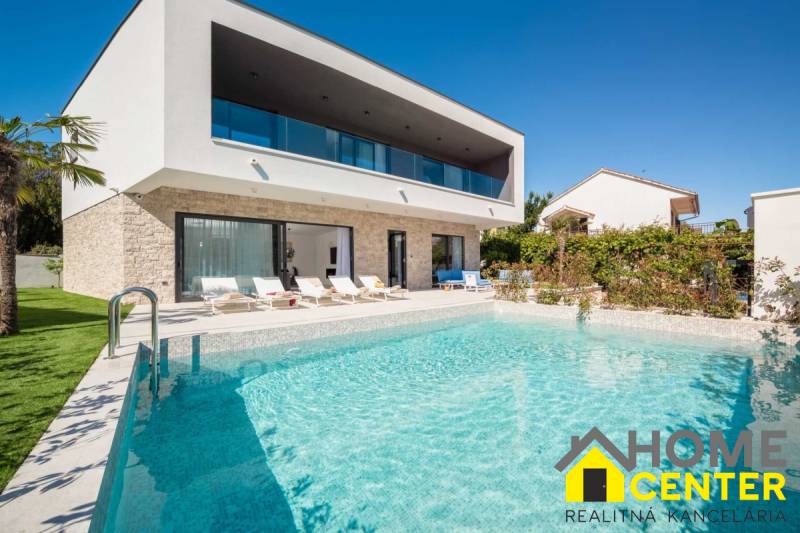 A villa in Bali with a pool and loungers, surrounded by greenery and a blue sky.