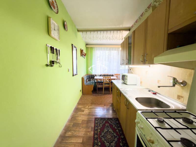 A kitchen in a 3-room apartment with a wooden decor floor and green walls.