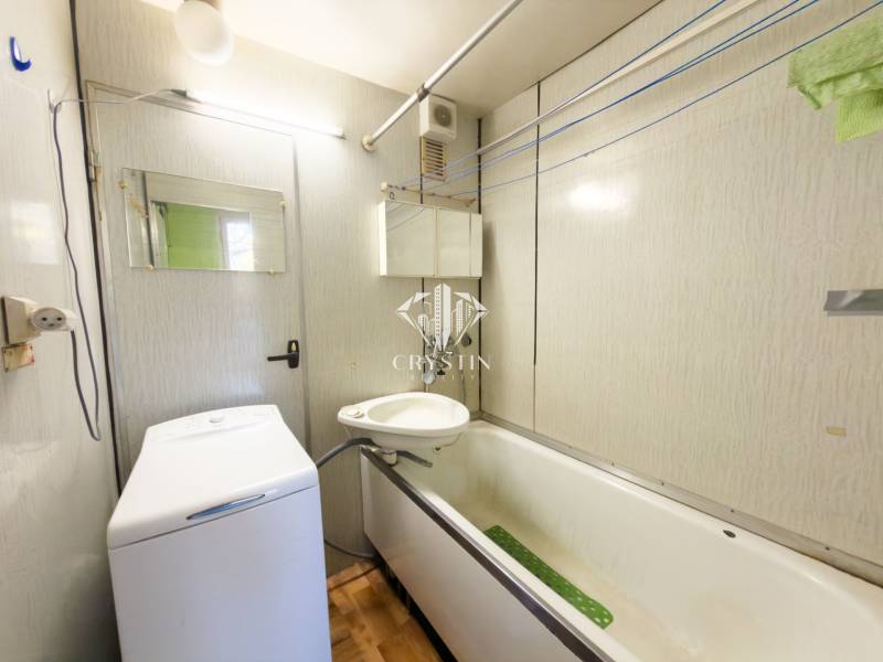 A bathroom in a 3-room apartment with a bathtub, sink, and washing machine, floor with wooden decor.
