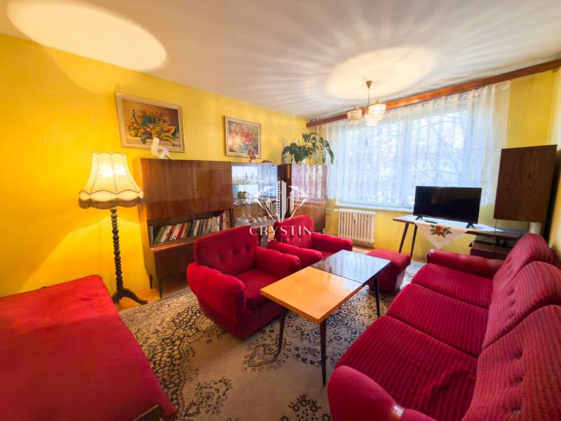 Living room of a three-room apartment with red sofas, carpet, wall decorations, wooden furniture.