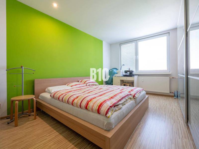 A bedroom in a 4-room apartment with a wood-patterned floor and a green wall.