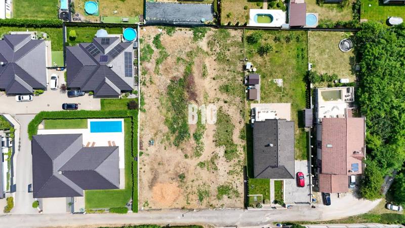 Aerial view of a construction site in Štitáre, surrounded by family houses and swimming pools.