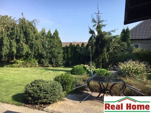 The garden of a family house in Čierna Voda with a lawn, trees, and outdoor seating.