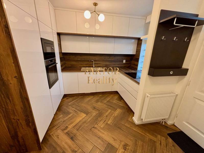 A kitchen in a 2-room apartment with a white kitchen unit and a floor with a wood decor.