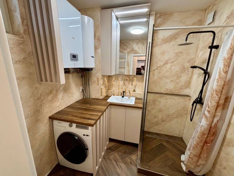 A bathroom in a 2-room apartment with a washing machine, a shower cabin, and a floor with a wooden decor.