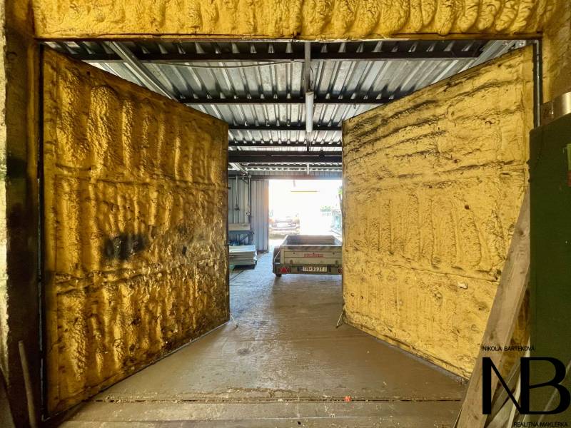 Commercial premises with open doors and a metal roof, a car is visible in the background.