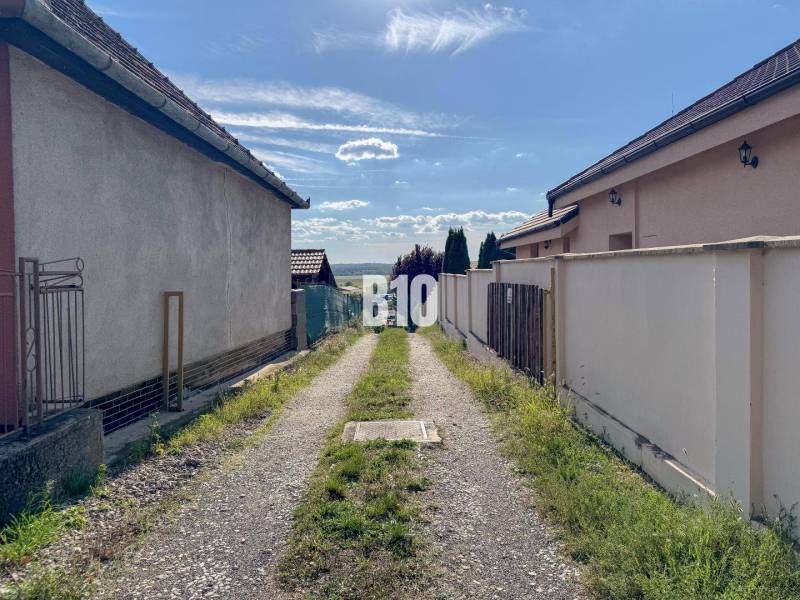 A narrow path between houses in the Pozemky - bývanie area, Nitra, leading to a landscape panorama.