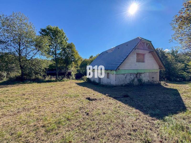 A cottage in Lackov on a sunny meadow surrounded by trees and a blue sky.
