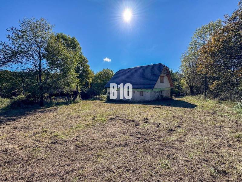 A cottage in Lackov surrounded by nature, grassy land, trees, and a clear sky.