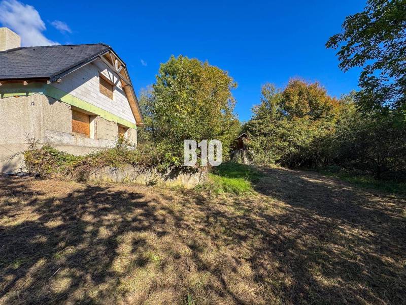 A cottage in Lackov surrounded by trees, with a grassy plot and a sunny sky.