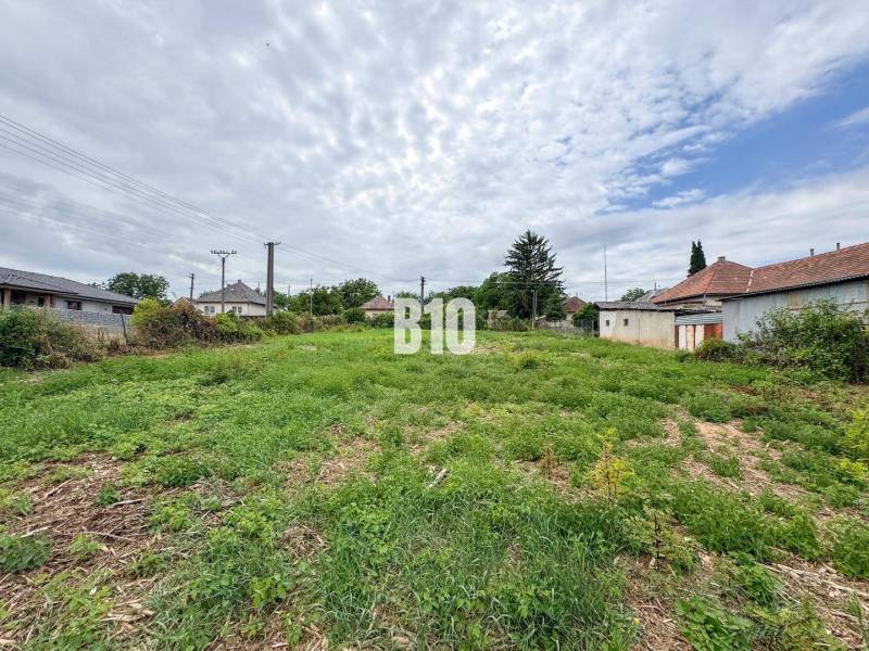 Plots for residential use in Bardoňovo, surrounded by houses and vegetation under a cloudy sky.