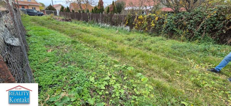 A residential plot in Tvrdošovce bordered by a fence, with a grassy surface and neighboring houses.