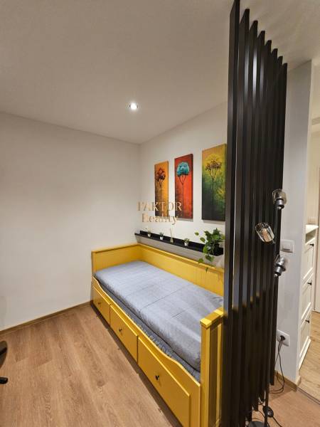 A studio apartment with a single bed, paintings of trees, and a floor with a wood decor.