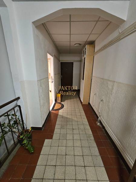 A hallway with tiles, white walls, leads to the door of a studio apartment.