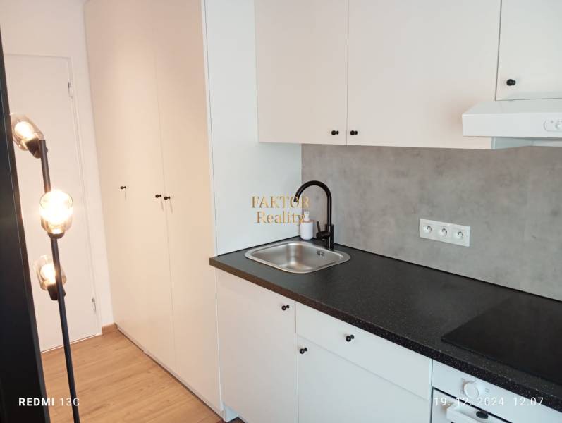 A kitchenette in a studio apartment with a wooden decor floor and spot lighting.
