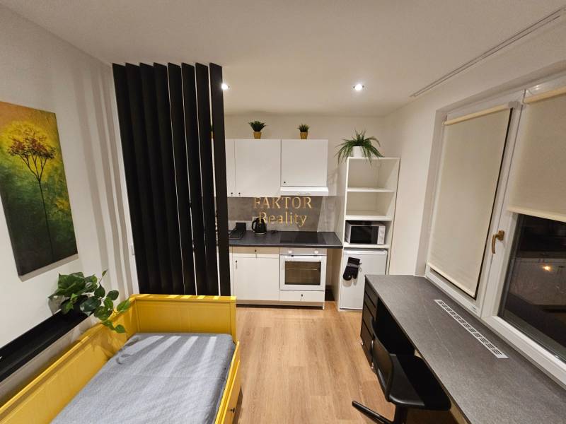 Studio apartment with a yellow bed, kitchen, table, and a wooden-patterned floor.