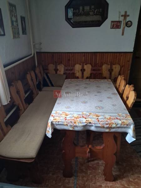 A dining room in a family house with wooden chairs and a table, the wall is adorned with paintings and a cross.