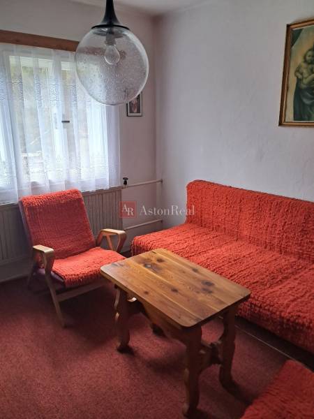 A room in a family house with red armchairs, a table, and curtain drapes.