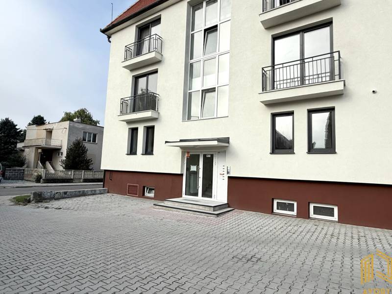 The building on Sadová Street in Senica with a white facade and a paved parking lot.