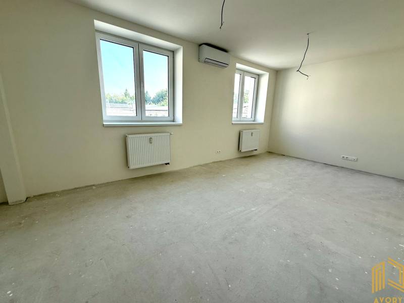 A spacious room in a 2-room apartment with large windows and neutral walls.
