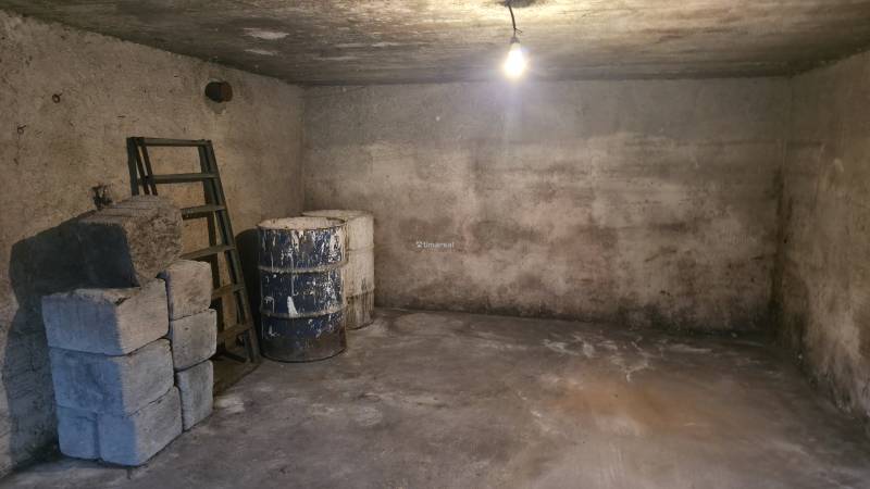 The basement of a family house with a concrete floor, you notice barrels and stairs.