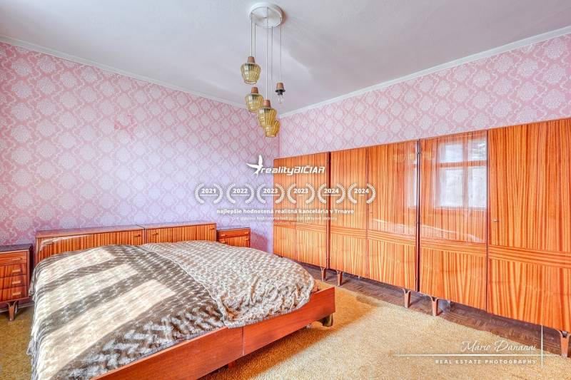 Bedroom in a family house with a large bed, cabinet, and ceiling chandelier.