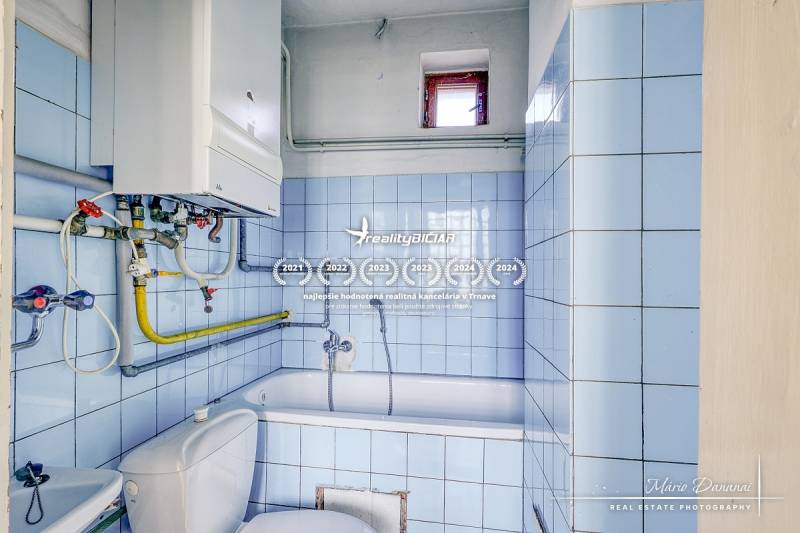 A bathroom in a family house with blue tiles, a bathtub, and a gas boiler.