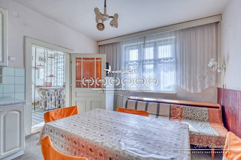 A dining room in a family house with a large window, a floral tablecloth, and orange chairs.