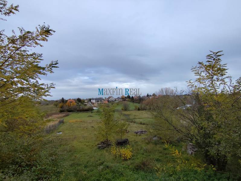 A plot of land in the town of Velky Bab, designated for residential use, surrounded by greenery and rural landscape.