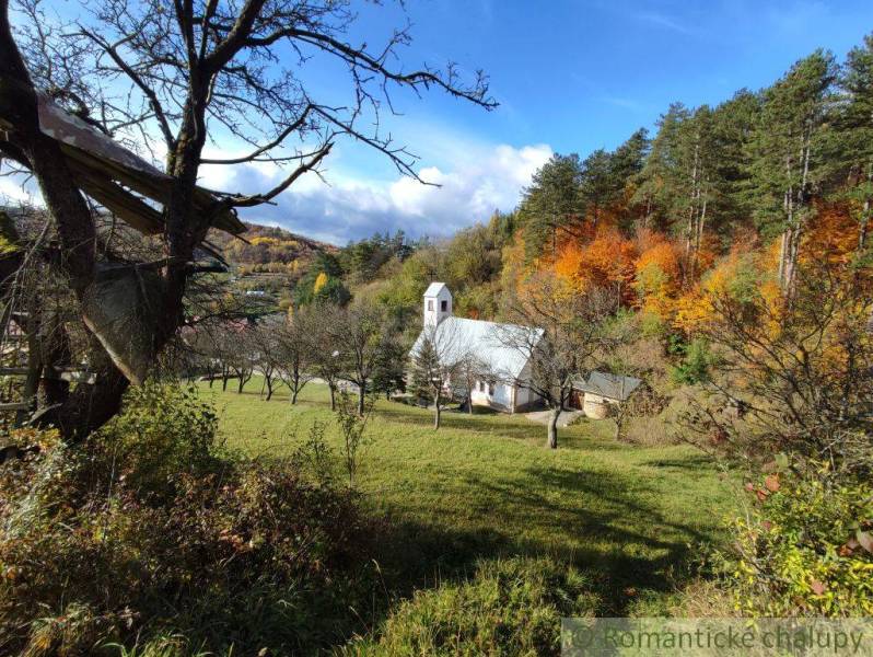 Autumn in the gardens of Hlboké nad Váhom with a small church among the trees, colorful forests in the background.
