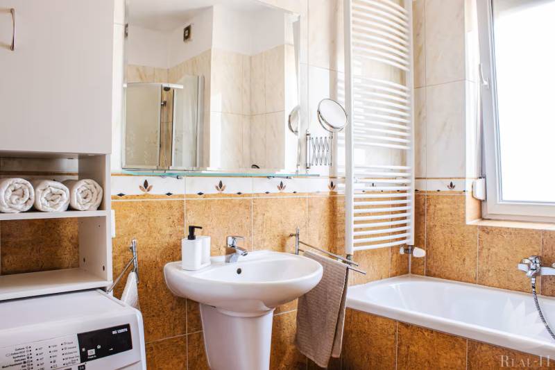 A bathroom in a 3-room apartment with a sink, bathtub, washing machine, and towel rack.