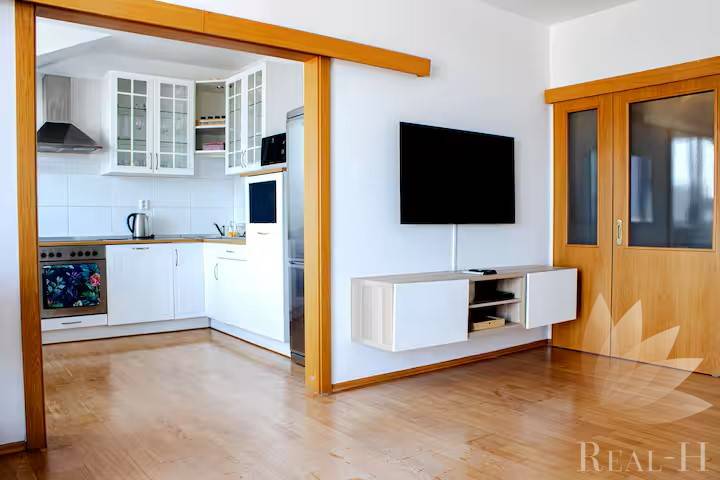 Living room in a 3-room apartment with a passage to the kitchen and a wall-mounted television.