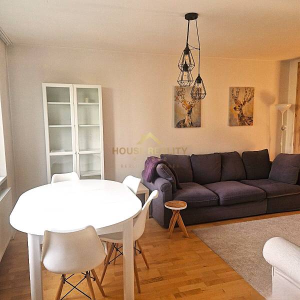 Living room with a sofa and a dining table in a 2-room apartment with wood-patterned flooring.
