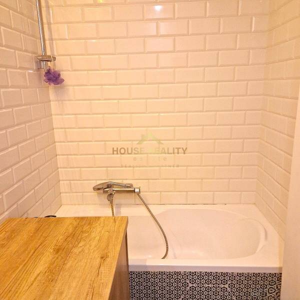 Bathroom in a 2-room apartment with white tiles and a bathtub.