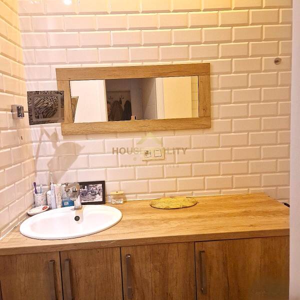 Bathroom in a 2-room apartment with white tiles and wooden decor.