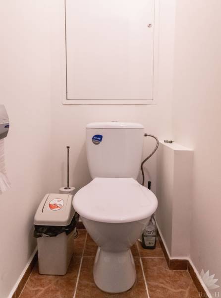 Bathroom with toilet, trash bin, and wooden decor flooring in a 2-room apartment.