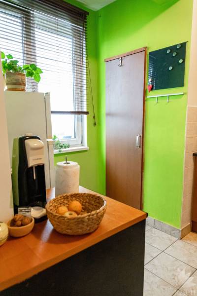 A kitchen in a 2-room apartment with wooden decor, green walls, and a window with blinds.