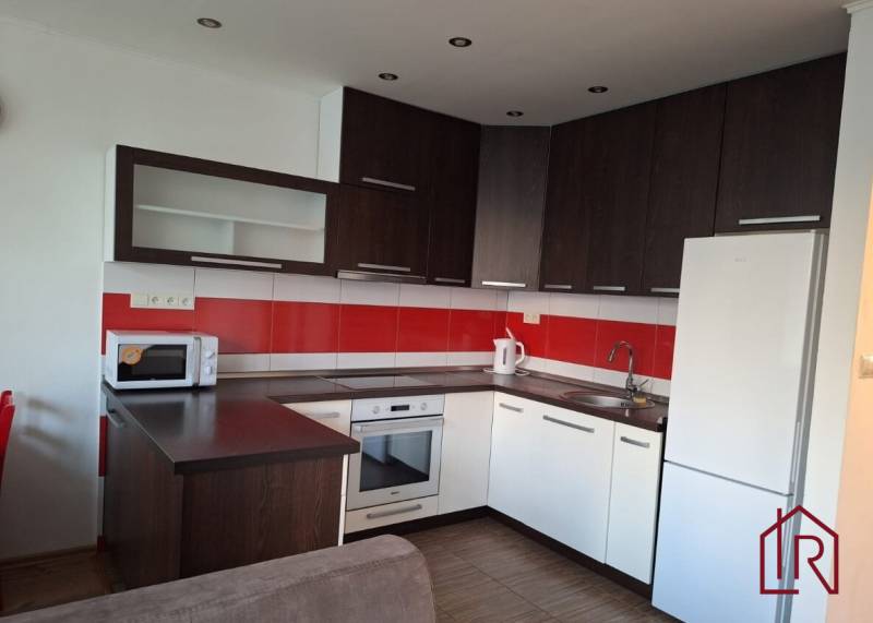 A kitchen in a 3-room apartment with white cabinets and red tiles, and a wooden decor floor.
