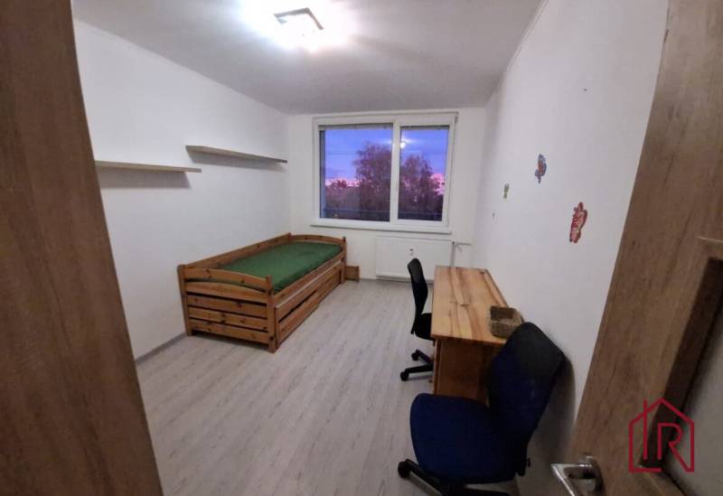 A room with a bed and a table in a 3-room apartment, with a floor featuring a wood decor.