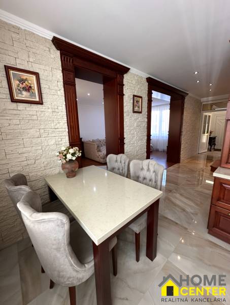 Dining area with a stone wall, white table, and upholstered chairs in a family house.